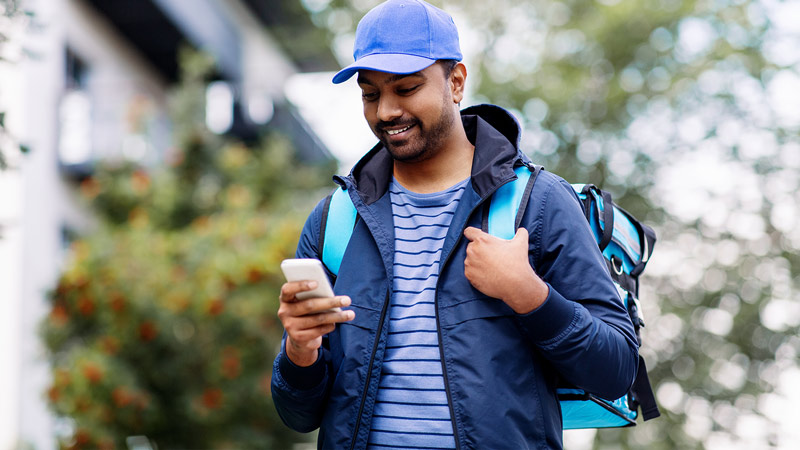 Smiling delivery man with bag using his smartphone