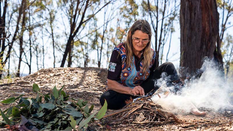 Leanne King of Wollombi Cultural Experiences sitting among twigs and smoke